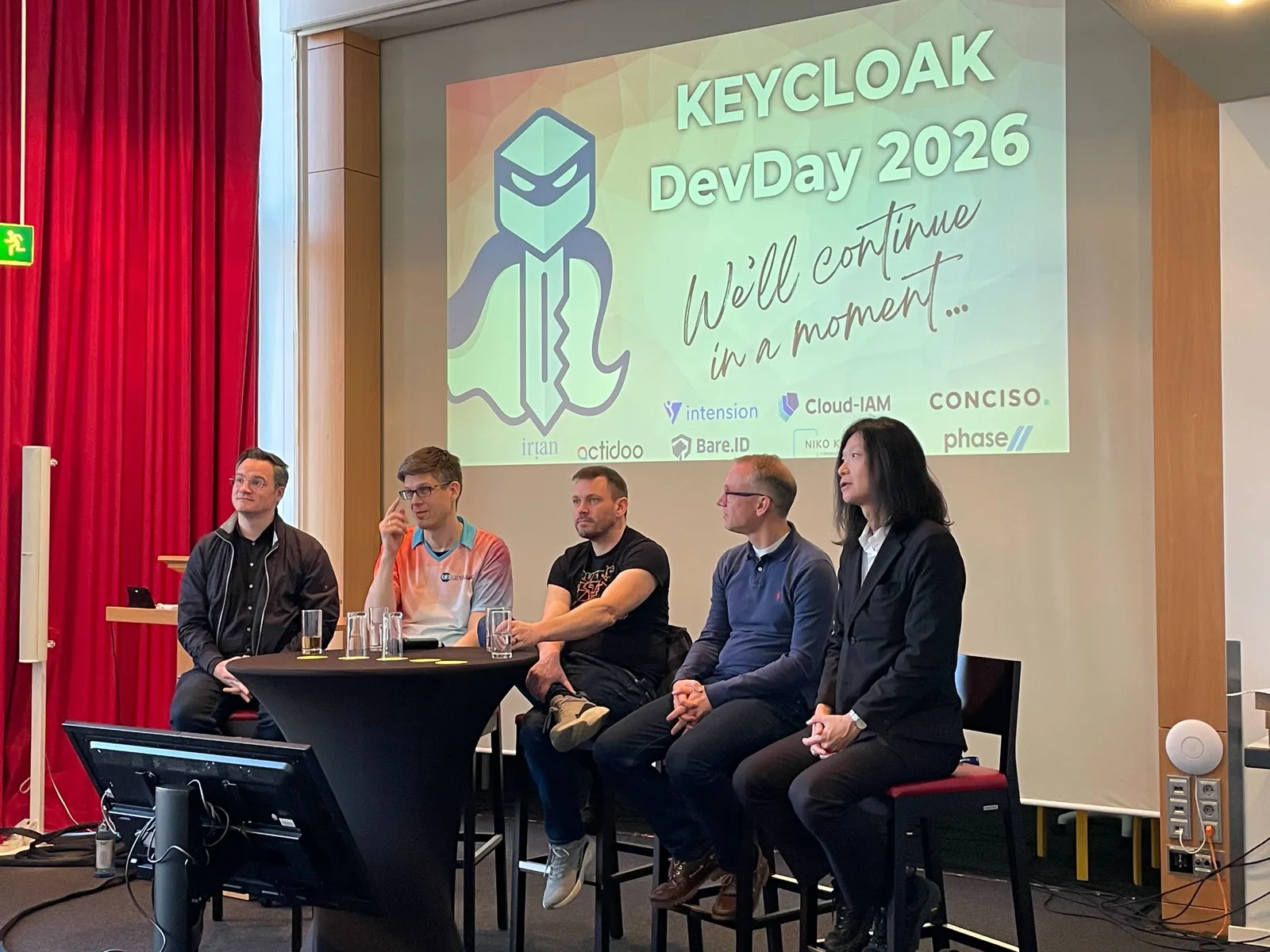 Un panel d'intervenants sur scène au Keycloak DevDay 2026, devant la slide des sponsors